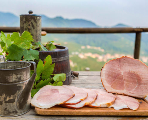 Foto con visibile un prosciutto aromatizzato al miele su una tavola allestita e sullo sfondo le colline di valdobiadene