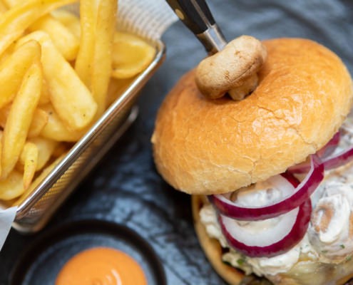 Fotografo food hamburger con cipolle su piatto nero e patatine fritte
